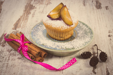Vintage photo, Muffins with plums and powdered sugar, cinnamon sticks on old wooden background, delicious dessert