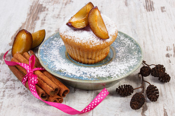 Muffins with plums and powdered sugar, cinnamon sticks on old wooden background, delicious dessert
