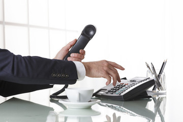 Businessman hands dialing out on a black deskphone - obrazy, fototapety, plakaty