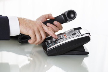 Close up of businessman hands dialing out on a black deskphone - obrazy, fototapety, plakaty