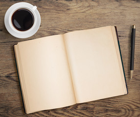 Open book with pen and coffee cup on old wooden table