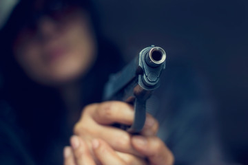 Woman pointing a gun at the target on dark background, selective focus