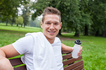young sporty man sitting on bench with bottle of water