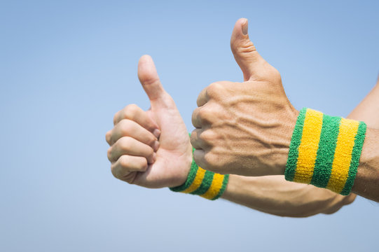 Brazilian athlete wearing Brazil colors wristbands holding two thumbs up against blue sky
