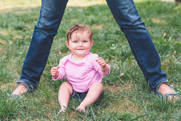 Baby sitting on a grass beside feet of mother