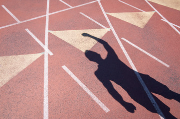 Athlete celebrating with a fist pump casting a shadow on a weathered red running track