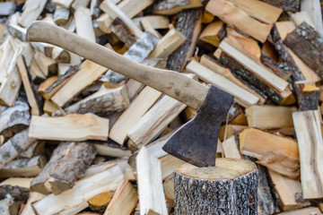 Closeup of an axe sticking in a chunk of firewood in front of a