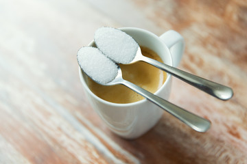 close up of white sugar on teaspoon and coffee cup