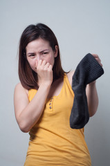Portrait of Asian woman in a yellow dress smelling socks foul.