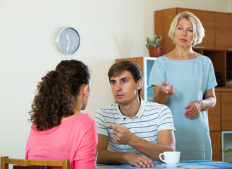 Upset female retiree watching adult kids quarrelling at home