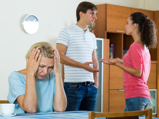 Mature woman watching young family couple quarrel at home