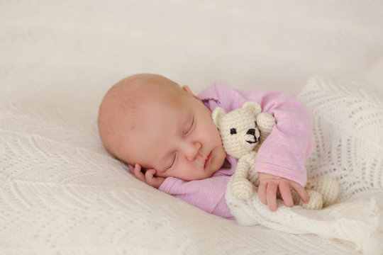 Neugeborenes Baby schläft zufrieden auf weißer Decke mit Teddy im Arm