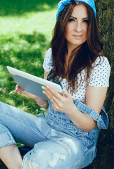 Obraz premium Brunette girl in park with tablet. Sunny day.