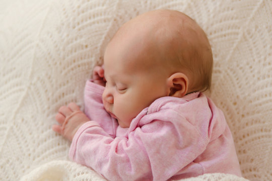 Neugeborenes Baby schläft entspannt im rosafarbenem Body