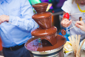 Fototapeta na wymiar Vibrant Picture of Chocolate Fountain Fontain on childen kids birthday party with a kids playing around and marshmallows and fruits dip dipping into fountain 
