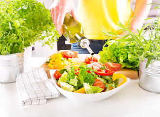 female hands pouring oil from bottle into the bowl of salad