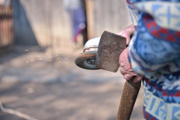 Close up of a man sharpen an ax using electric grinder. Sparks w