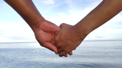 two hands holding together with the sea in the background
