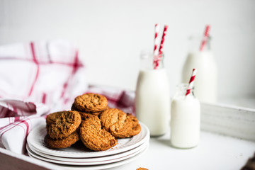 Oatmeal cookies with milk in jars on white wooden background