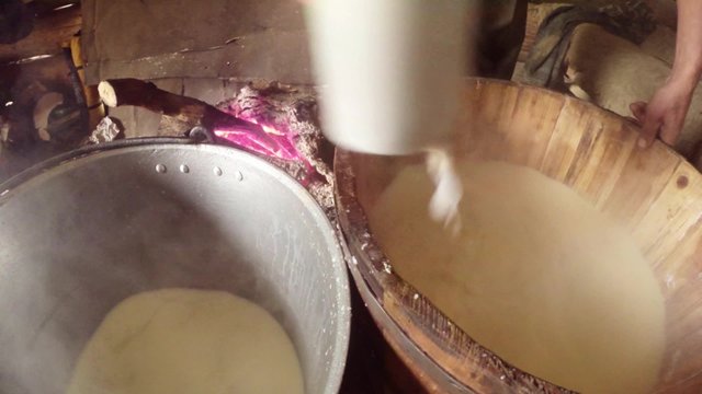 hand of the farmer collects cup liquid whey from wooden barrels with cheese