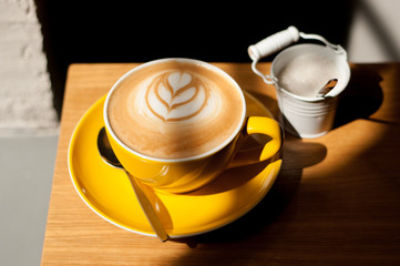 cappuccino with heart in yellow cup on wood table background overhead view cool shadows natural light