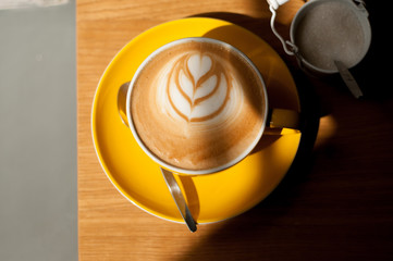 cappuccino with heart in yellow cup on wood table background overhead view cool shadows natural light