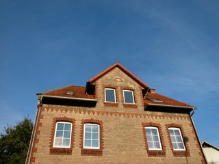 Dachgaube mit spitzem Giebel an der Fassade eines Altbau mit Backstein bei blauem Himmel und...
