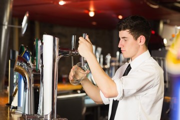 Barkeeper holding glass in front of beer dispenser at bar