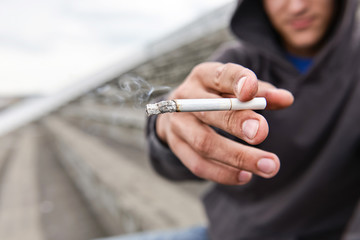 Hooded young man offers a cigarette to the viewer, outdoor