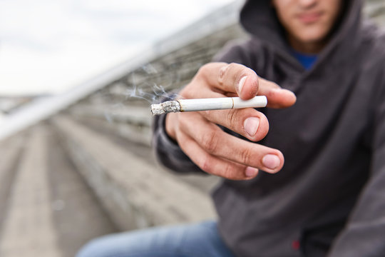 Hooded young man offers a cigarette to the viewer, outdoor