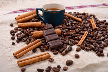 Cup of hot coffee with cinnamon sticks, bitten bar of chocolate