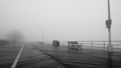 Fototapeta premium Black and white photo of a boardwalk disappearing into the fog. 