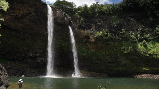 A hiker admiring Wailua Falls on Kauai, Hawaii, as seen from near the bottom of the falls.