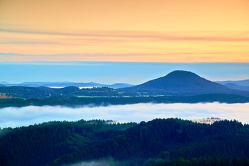 Blue foggy  deep valley after rainy night. Rocky hill bellow view point. The fog is moving between hills and peaks of trees, blue clouds in the sky.