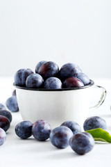 Fresh plums in cup on white wooden background