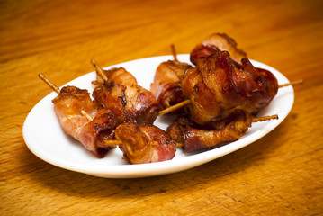 Rolls of slices of cooked bacon subject with a toothpick on a wh