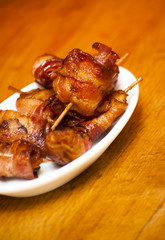 Rolls of slices of cooked bacon subject with a toothpick on a wh