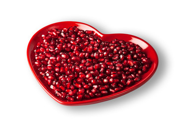 Red heart shaped plate full of delicious ripe juicy pomegranate seeds