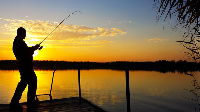 Young man fishing on a lake at sunset