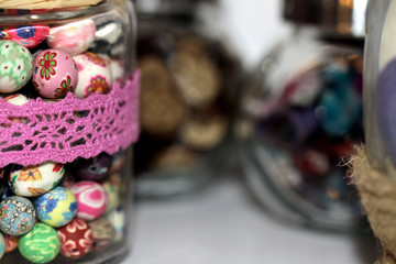 Nahaufnahme von bunten Zierknöpfen mit Gläsern im Hintergrund, horizontal