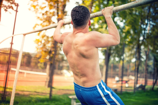 Muscular athletic man working out in park, training and doing pull ups. vintage dual color effect on photo