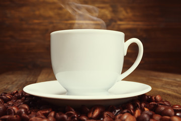 White cup of coffee and coffee beans on wooden table.