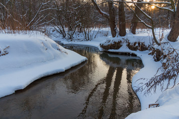 Winter landscape with a river in the woods in the evening at sunset