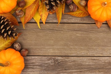 Autumn corner border of pumpkins, leaves and pine cones against a rustic wood background