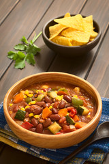 Vegetarian chili dish made with kidney bean, carrot, zucchini, bell pepper, sweet corn, tomato, onion, garlic, photographed with natural light (Selective Focus, Focus in the middle of the dish)