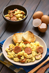 Scrambled eggs made with chorizo slices and onion on plate with toasted baguette slices, photographed with natural light (Selective Focus, Focus one third onto the plate)