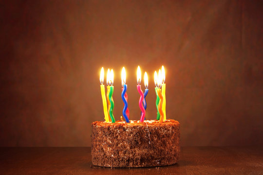Birthday chocolate cake with a lot of burning candles against brown background