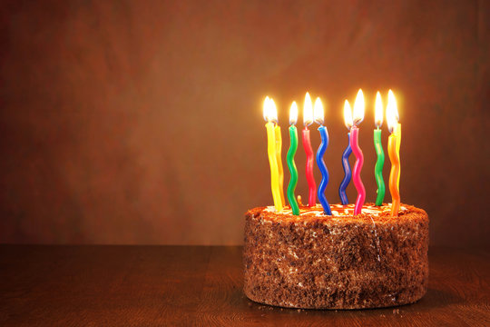 Birthday chocolate cake with burning candles on brown background