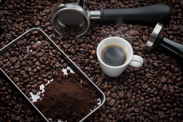 A cup of hot and fresh espresso coffee lay on many roast coffee beans also see an espresso machine group head.
