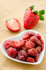 Dried strawberries in white bowl and fresh strawberry.